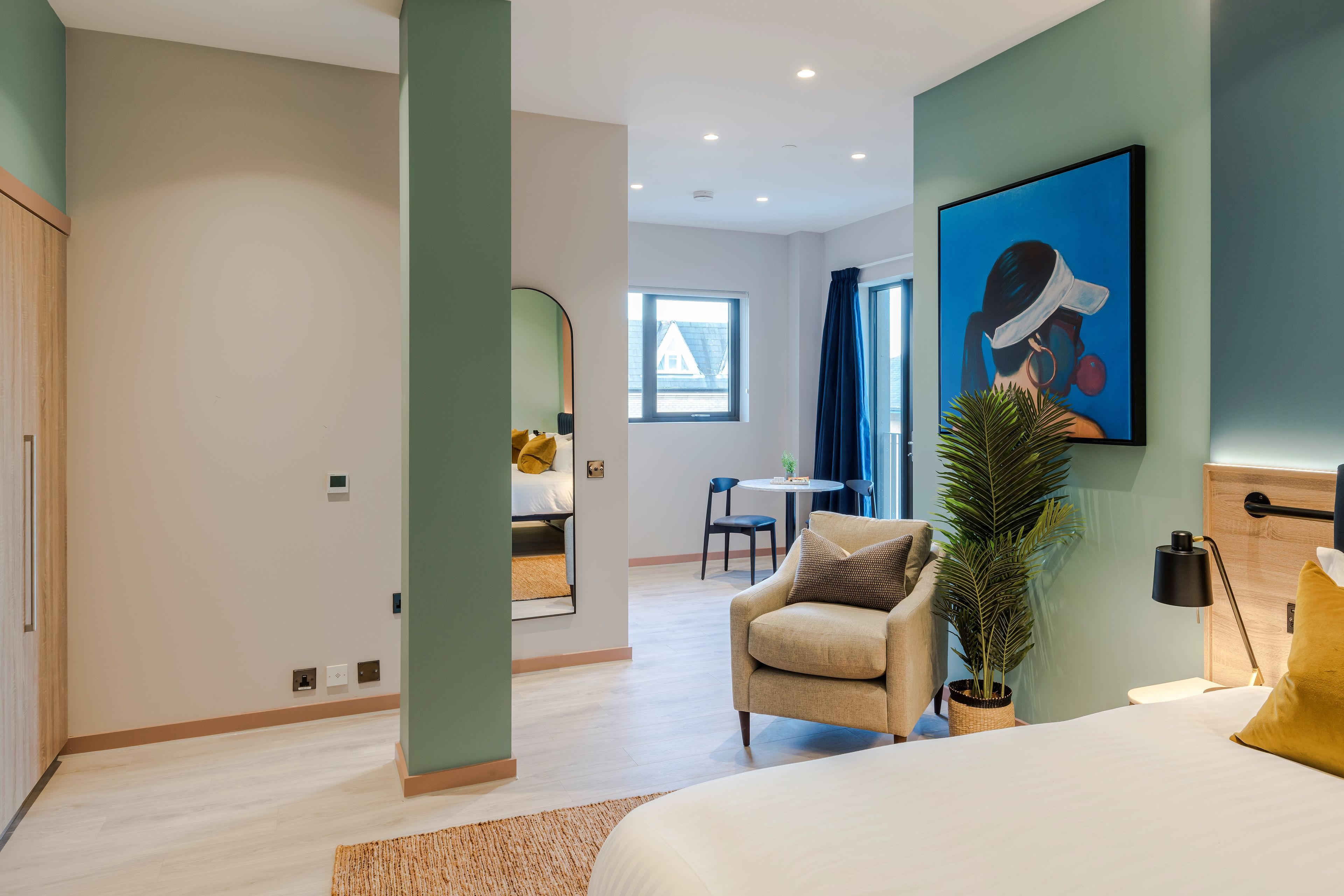 A modern hotel room with a bed, a sofa, a desk, and a large window.