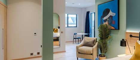 A modern hotel room with a bed, a sofa, a desk, and a large window.