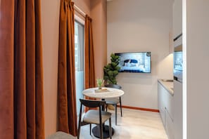 Una cocina compacta con comedor, que incluye una mesa redonda, dos sillas, una planta en maceta y un televisor de pantalla plana montado en la pared.