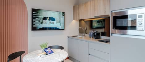 A modern kitchen with a built-in microwave, a coffee maker, and a TV mounted on the wall displaying a welcome message.