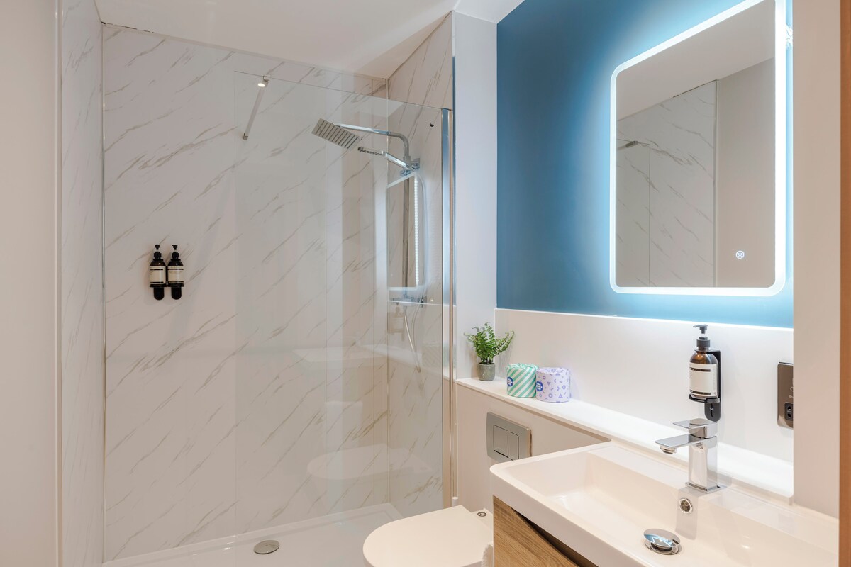 Une salle de bain moderne avec une douche à parois de verre, un lavabo blanc et un mur d’accent bleu.