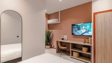 A modern hotel room with a bed, a desk with a chair, a television, and a wardrobe.