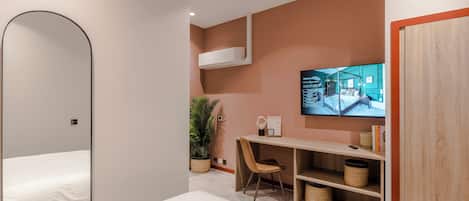 Una habitación de hotel moderna con cama, escritorio con silla, televisor y armario.