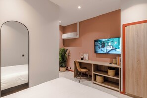 Una habitación de hotel moderna con cama, escritorio con silla, televisor y armario.