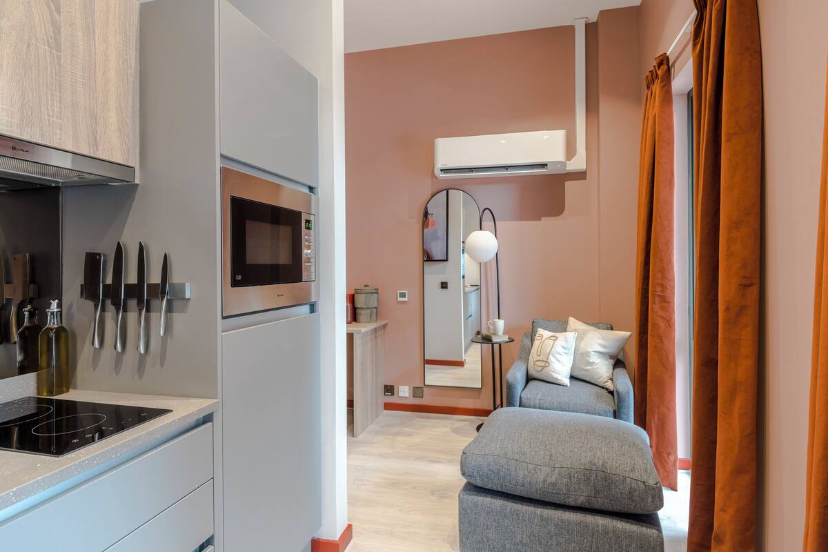Une cuisine moderne équipée d’un four à micro-ondes, d’une cuisinière et de couteaux fixés au mur, d’un canapé avec des coussins et d’un appareil de climatisation.