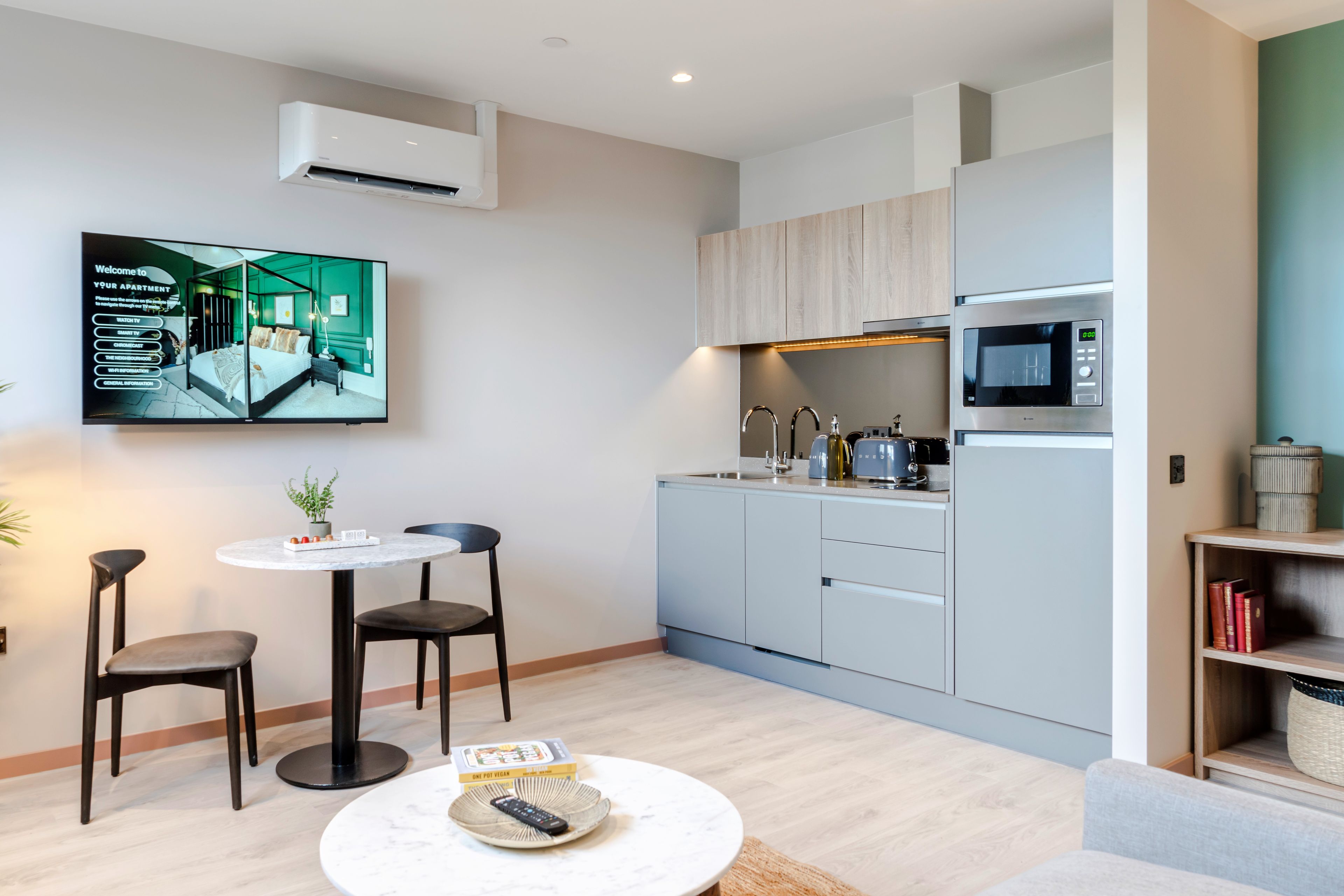 A modern apartment with a kitchen, dining area, and a flat-screen TV mounted on the wall.