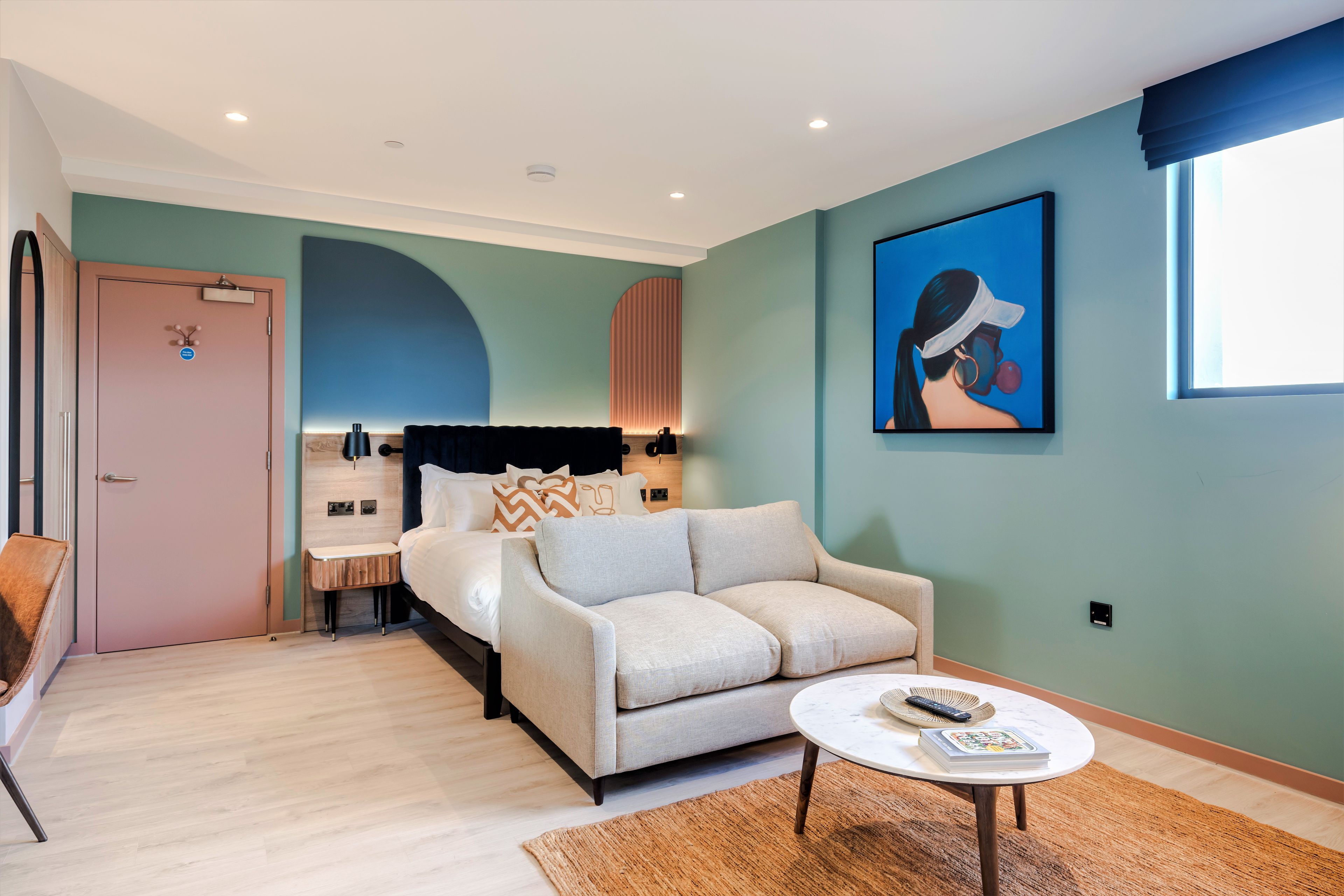 Una habitación de hotel moderna con una cama, un sofá, una mesita de centro y un cuadro en la pared.