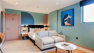 Una habitación de hotel moderna con una cama, un sofá, una mesita de centro y un cuadro en la pared.