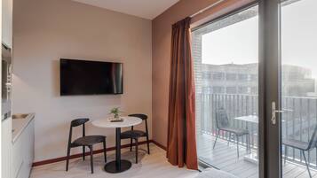 A modern room with a flat-screen TV mounted on the wall, a small round table with two chairs, and a balcony with a glass door.