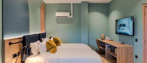 Un dormitorio moderno con cama, mesita de noche, televisor y un escritorio con silla.