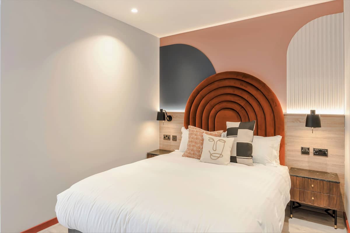 Une chambre à coucher moderne avec un grand lit, une tête de lit circulaire originale et une table de chevet avec une lampe.