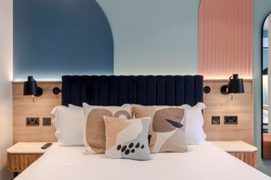 Un lit bien fait, agrémenté de coussins décoratifs, avec une tête de lit en bois et des lampes de chevet.