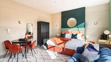 Una habitación de hotel con una cama, un espejo redondo, una mesa de comedor con sillas y un sofá azul.