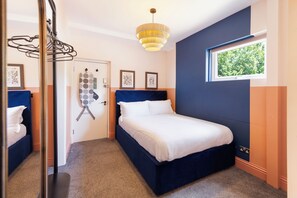 Een slaapkamer met een bed, een raam, een deur en een hangende lamp.