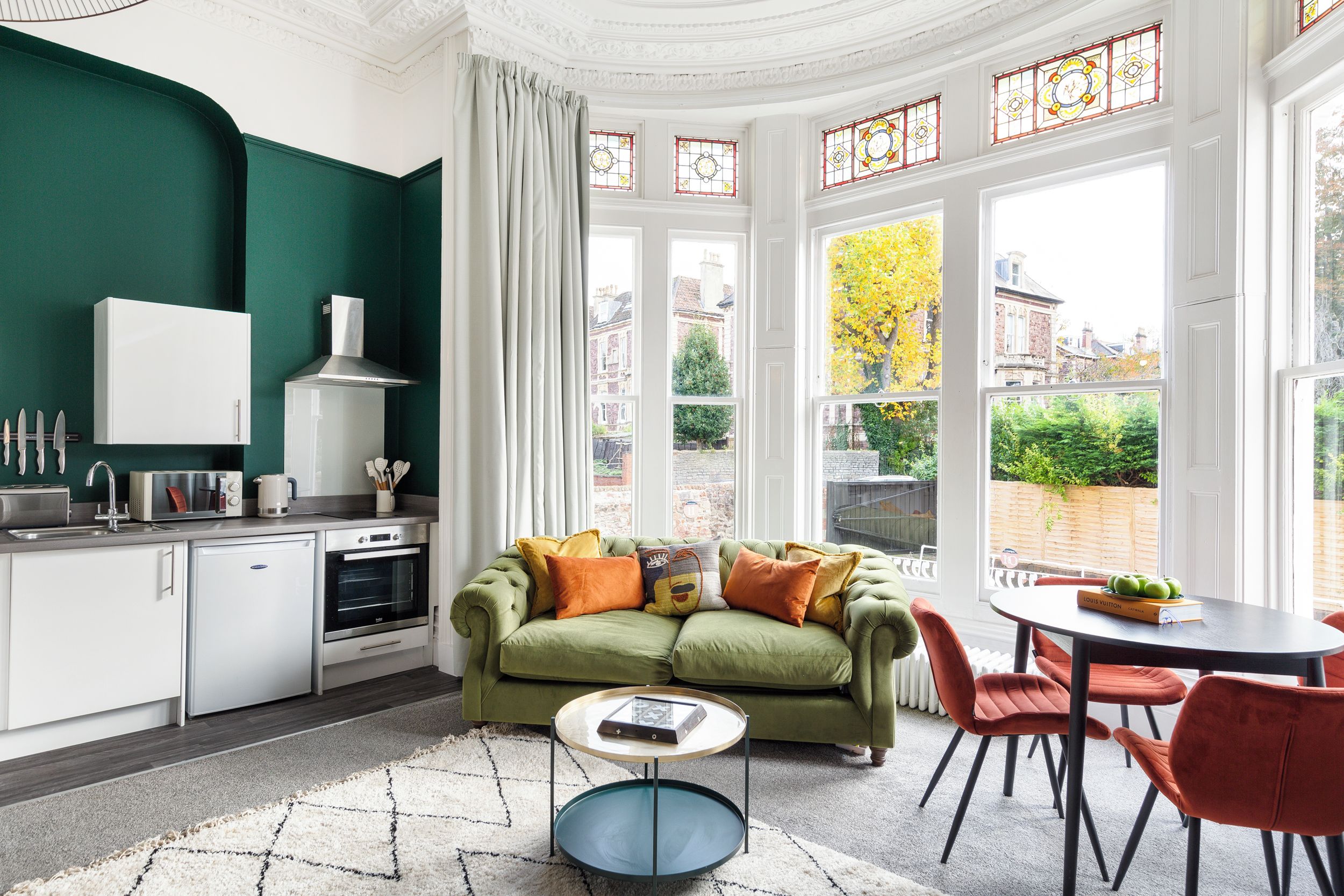 A modern kitchen with white cabinetry, a green sofa, and a dining table with red chairs.