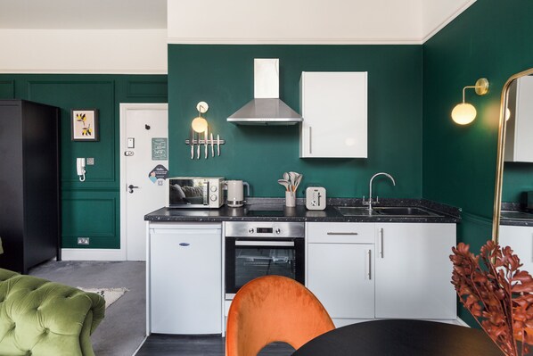 Una cocina compacta con armarios blancos, una campana extractora de acero inoxidable y una encimera negra.