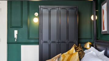 A bedroom with a dark wooden wardrobe, a white radiator, a bedside table with a lamp, and a bed with multiple pillows.