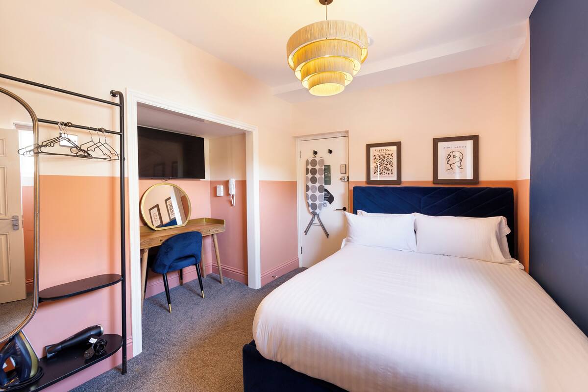 Een hotelkamer met een bed, een bureau met stoel, een kledingkast en een spiegel.