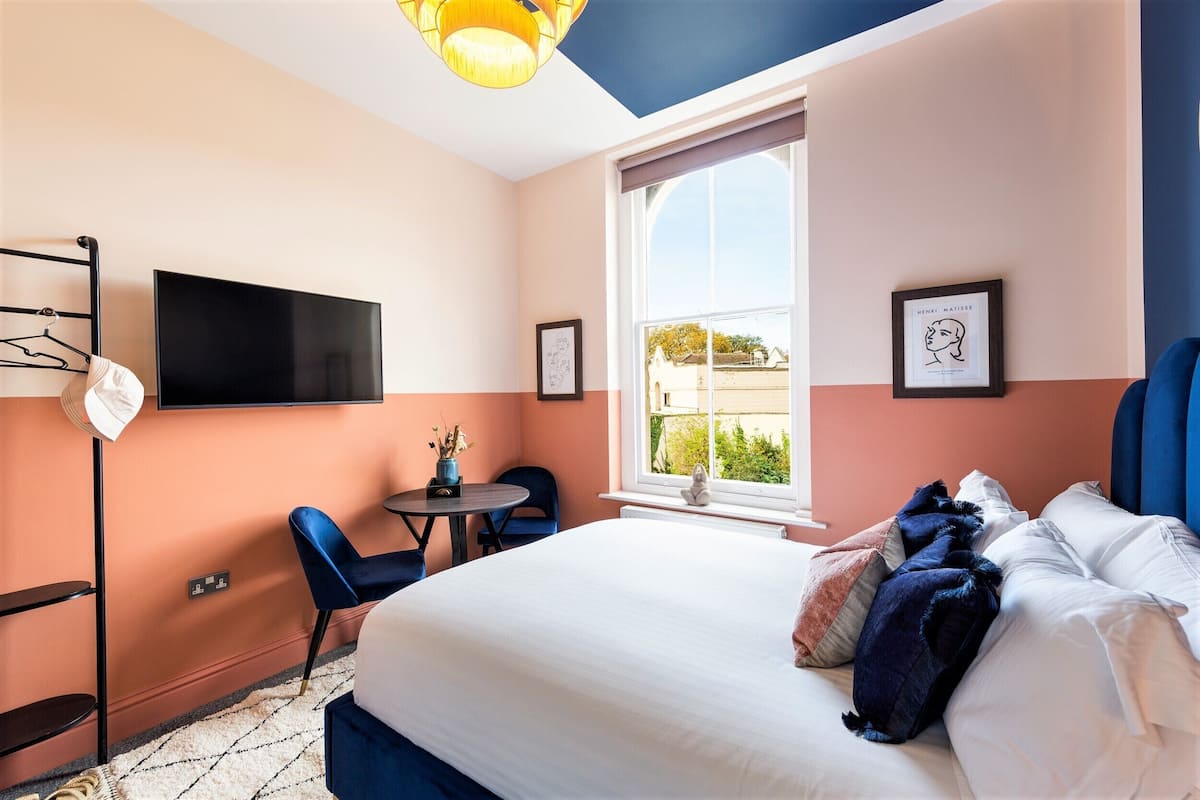 Een slaapkamer met een bed, een bureau, een stoel, een televisie en een raam met uitzicht.