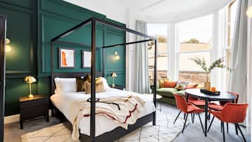 A modern bedroom with a four-poster bed, a green accent wall, and a view of the outdoors through large windows.