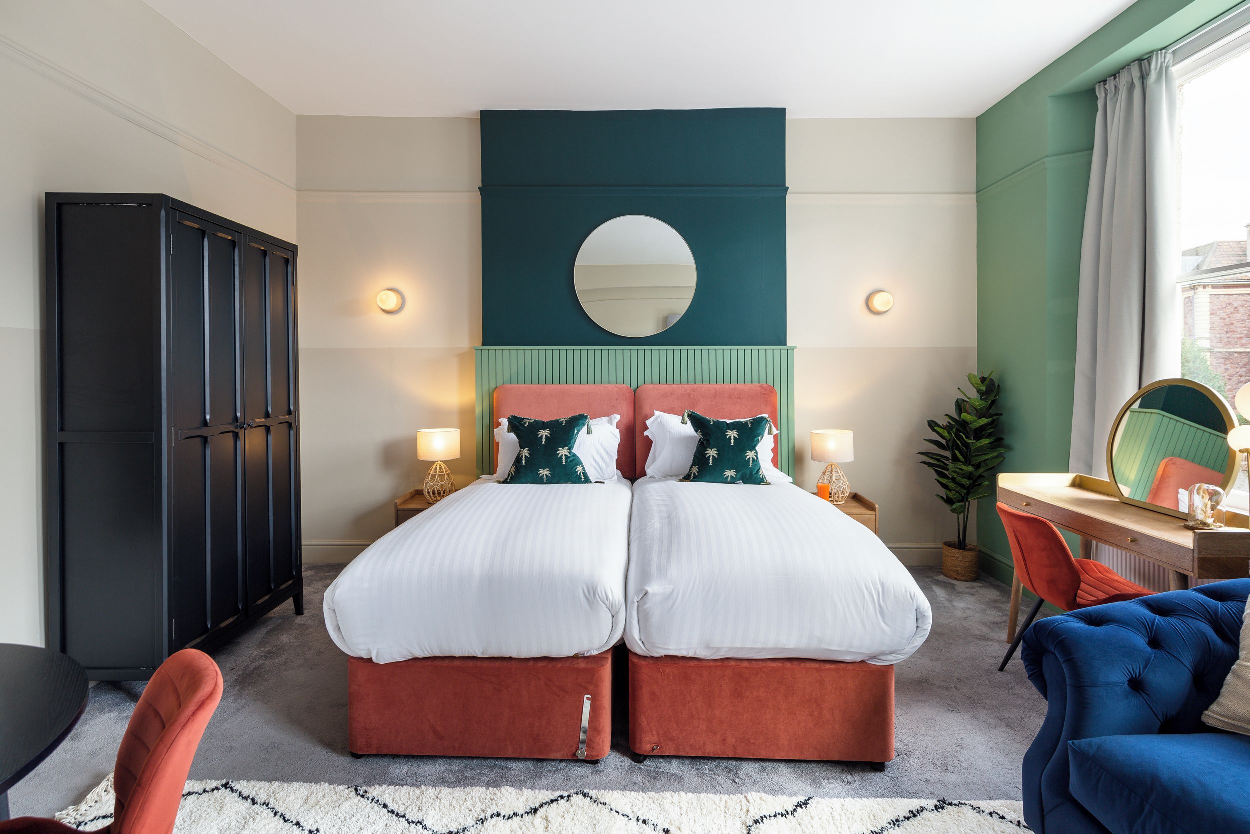 A double bed with two nightstands, a desk with a chair, a wardrobe, and a mirror.