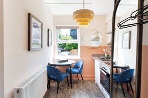 Une cuisine compacte avec un coin repas, comprenant une table ronde, des chaises bleues, un luminaire suspendu et une vue par la fenêtre.