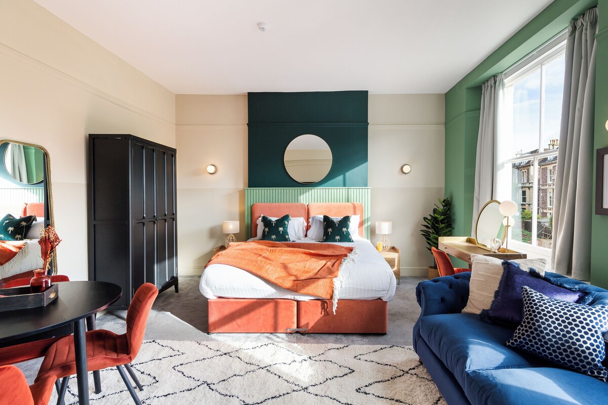 Une chambre moderne avec un grand lit, un canapé bleu, une table à manger et un miroir.