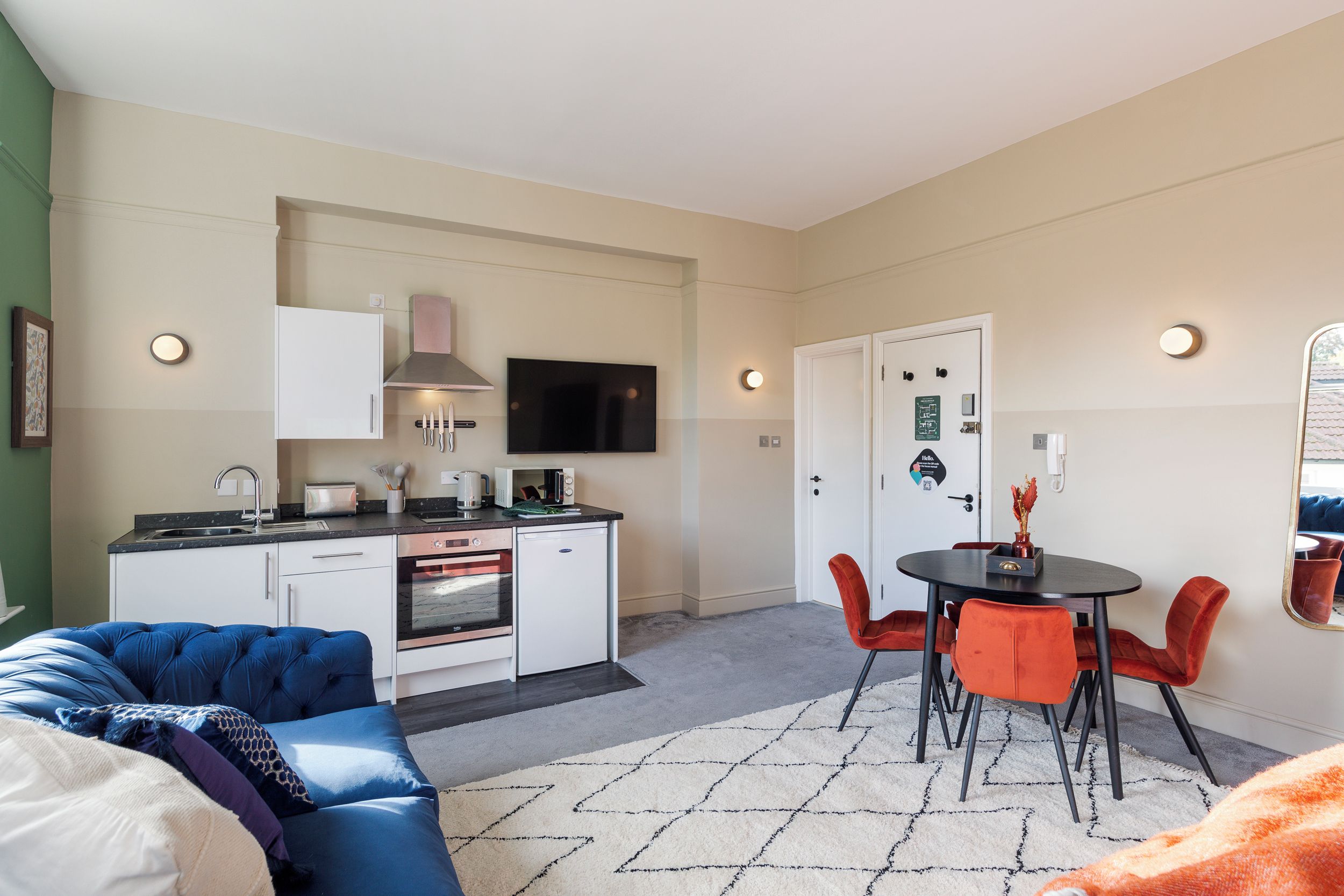 A compact living space with a kitchenette, a dining area with red chairs, and a sofa.