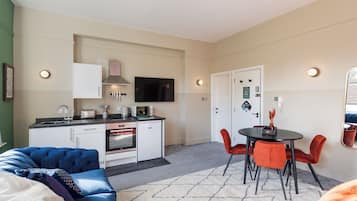 A compact living space with a kitchenette, a dining area with red chairs, and a sofa.