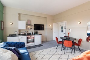 A compact living space with a kitchenette, a dining area with red chairs, and a sofa. - Clifton House - Your Apartment (Bristol)