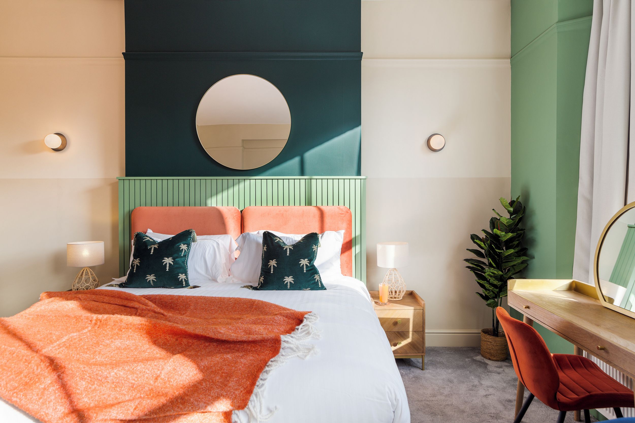 A bedroom with a bed, bedside table, chair, and a desk with a mirror.