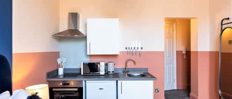 A compact kitchenette with a microwave, toaster, and small oven, a sink, and a cabinet above.