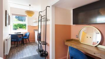 A room with a wooden desk, a large mirror, a TV, and a seating area with chairs.