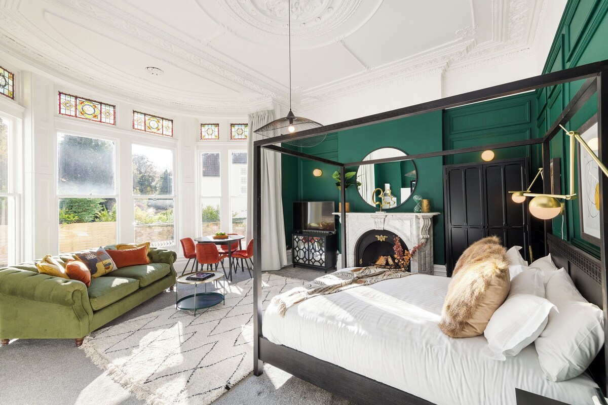 Une chambre spacieuse avec un grand lit, un canapé vert et un coin repas comprenant une table et des chaises.