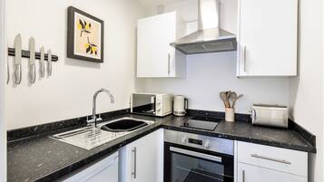 A compact kitchen with white cabinets, a black countertop, a microwave, a toaster, and a sink.