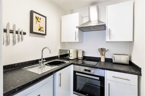 A compact kitchen with white cabinets, a black countertop, a microwave, a toaster, and a sink.