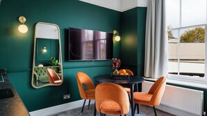 Une pièce aux murs de couleur turquoise, avec une table ronde, quatre chaises orange, un téléviseur à écran plat et une fenêtre avec des rideaux.