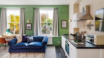 A modern kitchen with a blue sofa, a dining table, and a large window with curtains.