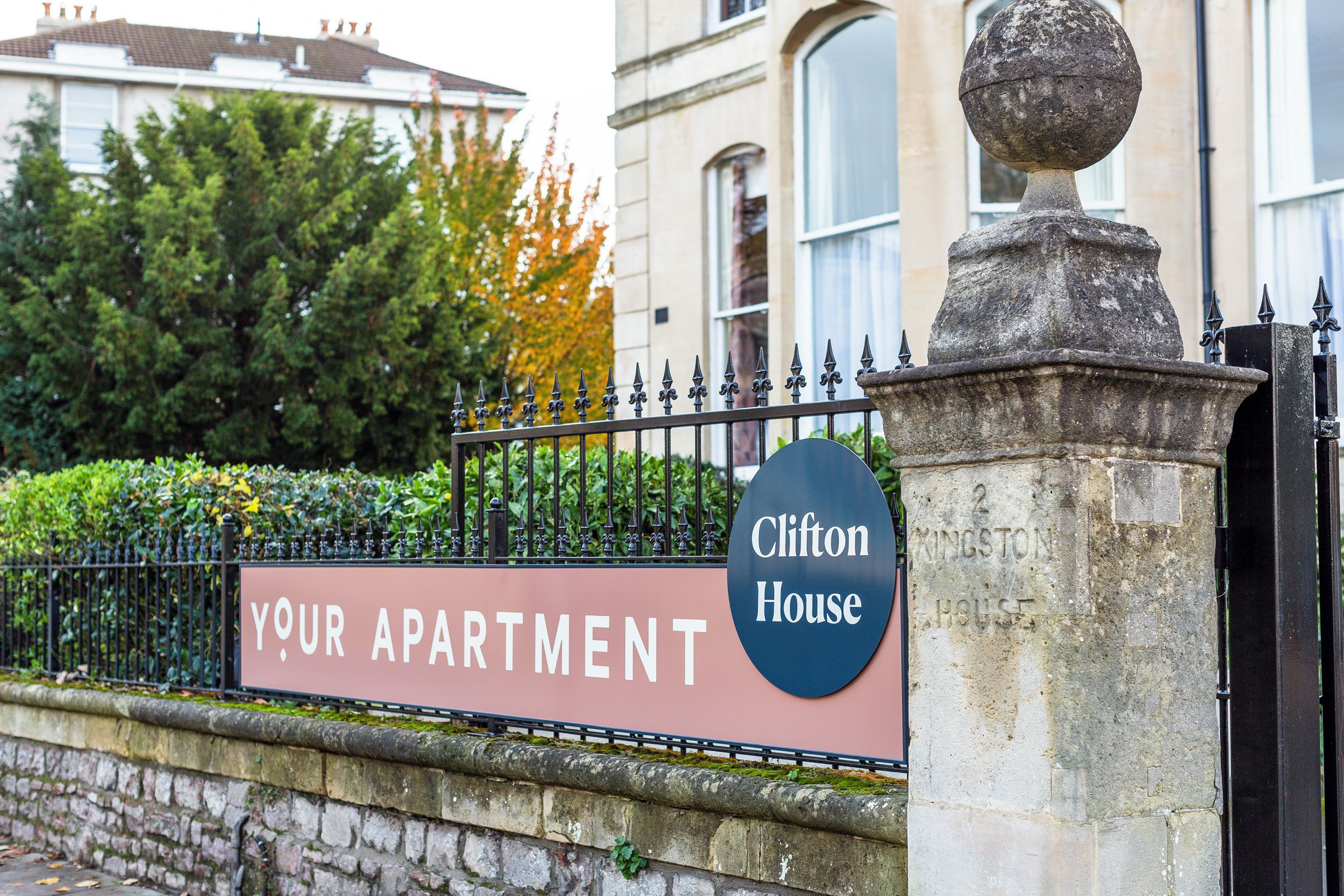 A sign for 'Clifton House' with a stone pillar and a wrought iron fence.