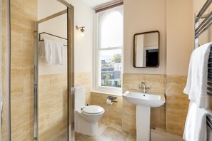 Een moderne badkamer met een douchecabine van glas, een toilet, een wastafel en een raam met uitzicht op gebouwen.