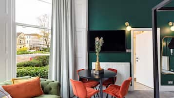 A room with a dining table, chairs, a sofa, and a TV mounted on the wall.