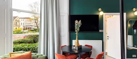 A room with a dining table, chairs, a sofa, and a TV mounted on the wall.