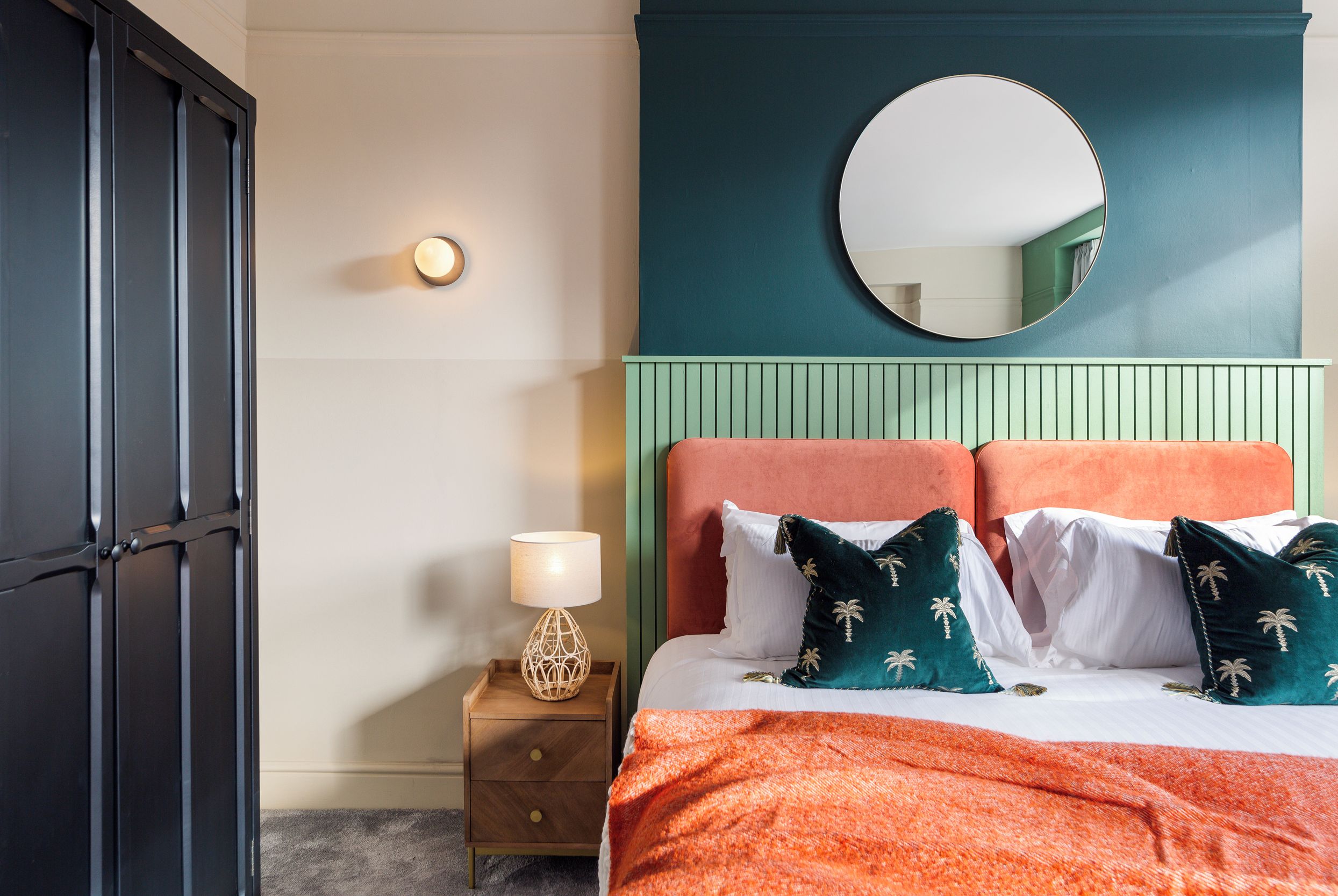 A bedroom with a bed, a nightstand, a lamp, a mirror, and a wardrobe.