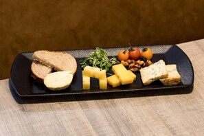 Une assiette rectangulaire noire sur laquelle sont disposés divers aliments, notamment des tranches de pain, du fromage, des noix et des tomates.