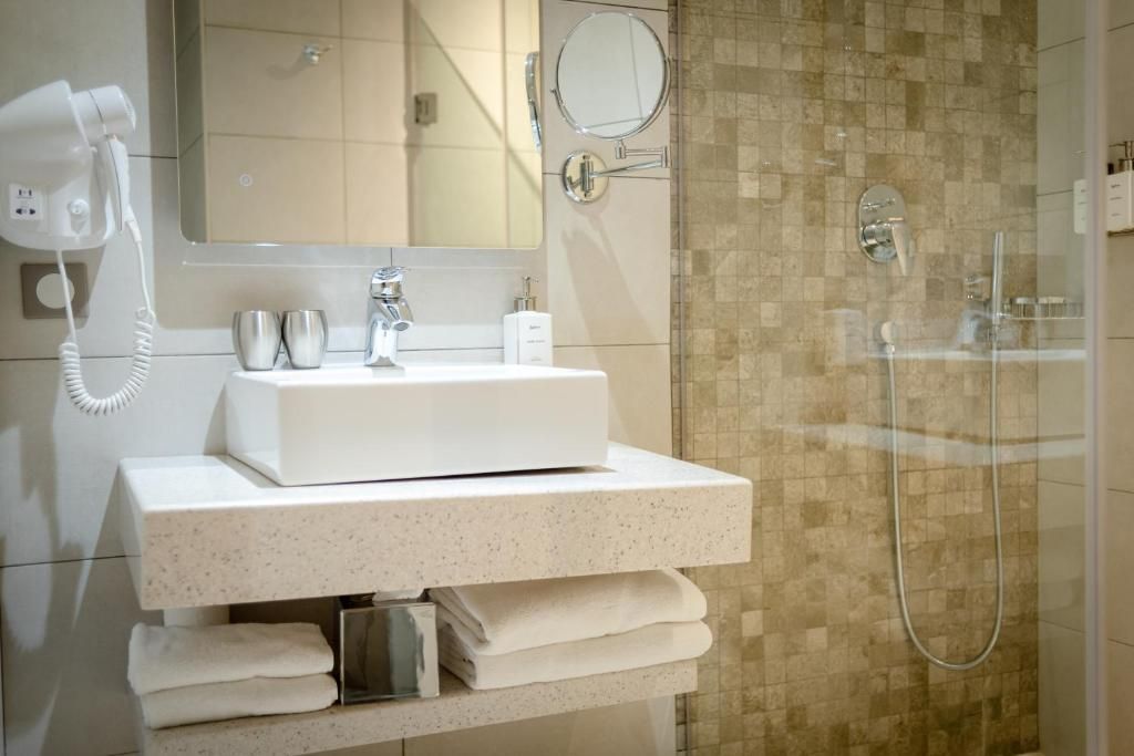 Un baño moderno con lavabo blanco, secador de pelo, espejo y ducha.