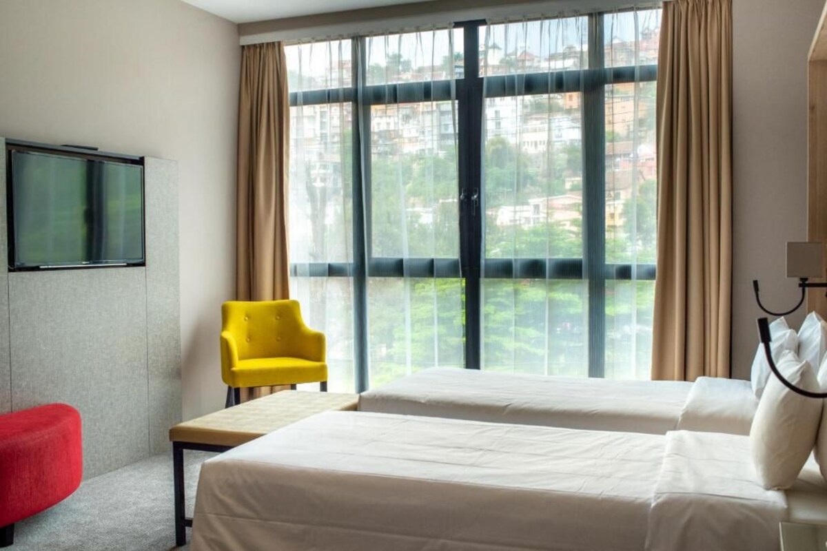 Een hotelkamer met twee bedden, een televisie, een gele stoel en een rode poef.