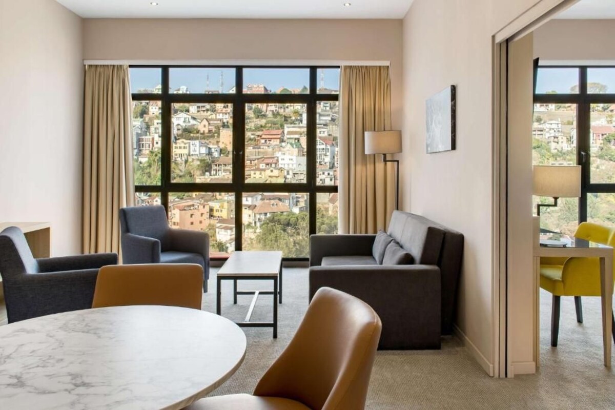 Een moderne hotelkamer met een groot raam met uitzicht over de stad, een ronde marmeren tafel en modern meubilair.