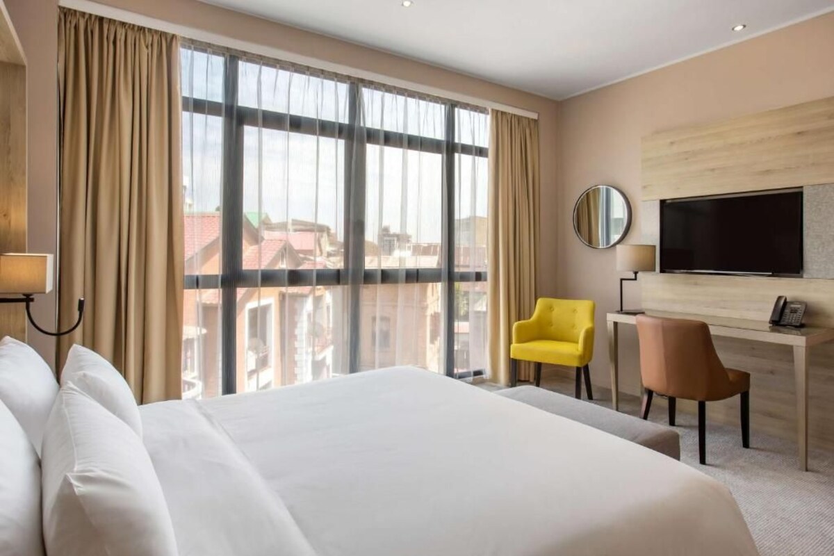 Een hotelkamer met een groot bed, een bureau, een televisie en uitzicht op gebouwen.