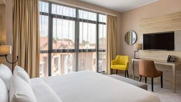 Habitación de hotel con una cama grande, un escritorio, un televisor y vistas a edificios desde la ventana.