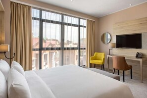 Een hotelkamer met een groot bed, een bureau, een televisie en uitzicht op gebouwen.